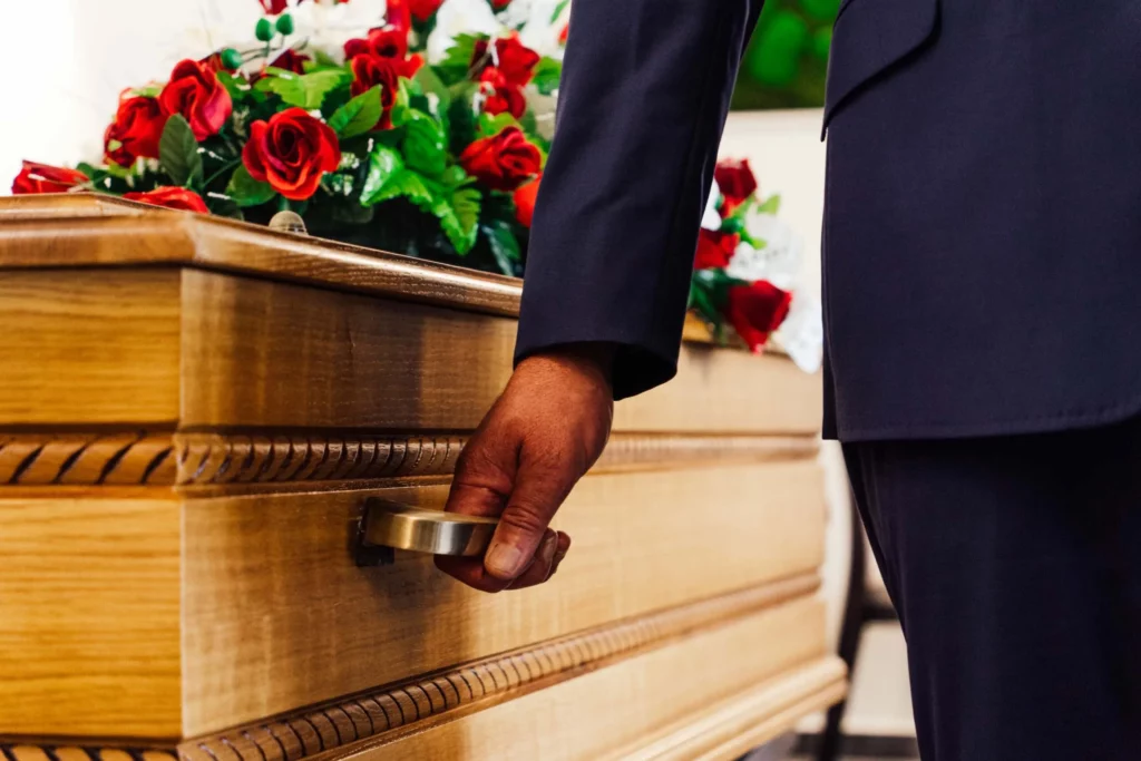 Main d'un conseiller funéraire ouvrant la poignée d'un cerceuil en bois orné de roses rouges